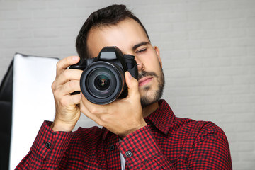 Young photographer with camera and studio equipment on grey background