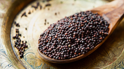 Black Mustard Seeds on wooden spoon and brass plate, Indian spices, macro.