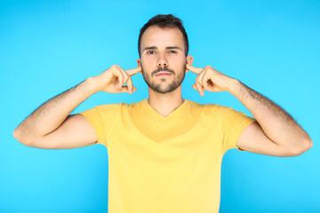 Naklejka premium Portrait of young man closing ears by fingers on blue background
