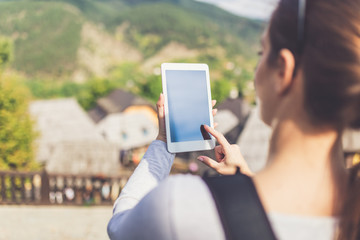 Female tourist holding blank screen digital tablet device against beautiful mountain village....