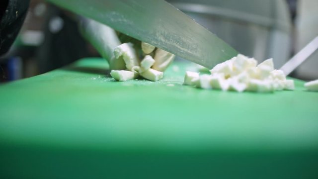 Close up of a cook cutting fresh mozzarella cheese on green teflon cutting board