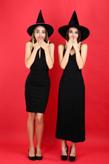 Two young women in black halloween costumes on red background