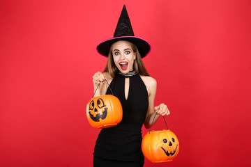 Beautiful woman in black costume holding halloween pumpkin buckets on red background