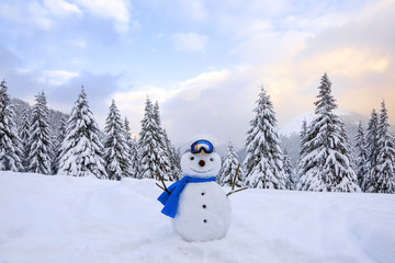 Funny snowman in ski glasses and blue scraf. Winter landscape with trees in the snowdrifts, the...