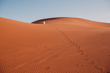 Fototapeta na wymiar A man walks through the desert leaving a chain of tracks