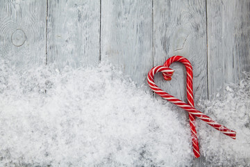 Christmas heart of two red lollipops on a wooden snowy gray background. Christmas background, top view and copy space