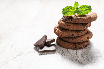Fresh homemade chocolate cookies with dark chocolate pieces and mint leaves on rustic marble table, copy space for your text.