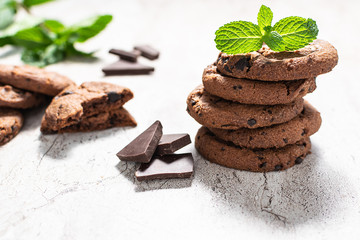 Fresh organic homemade chocolate cookies with mint leaves and pieces of dark chocolate on marble textured table.of 