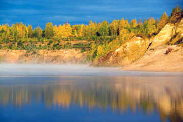 The shore of the misty lake in the early morning lit by the bright sun . Autumn landscape.