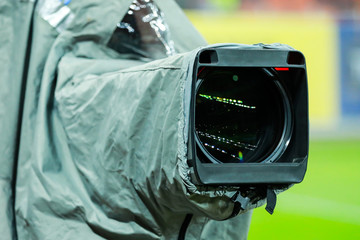 Details of a professional television camera, with rain cover, live broadcasting a soccer game.