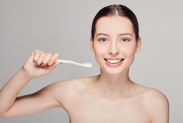 Young pretty girl with a toothbrush in her hands nearly her face with white teeth, with brown hair with clean fresh skin posing on a gray studio background,