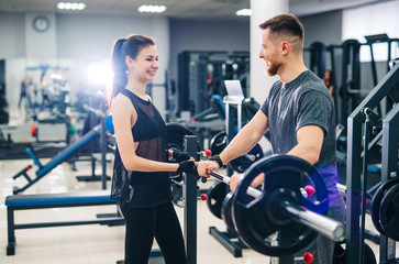Sport, bodybuilding, lifestyle and people concept - young man and woman with a barbell. Trainer and...
