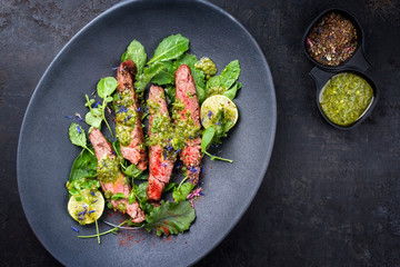 Barbecue wagyu hanging tender steak with chili, lettuce and chimichurri sauce as top view on a modern design plate