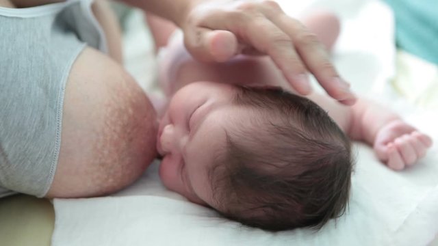 Newborn baby lying back near mother breast, breastfeeding. Close up view at Caucasian baby and female hand covering infant head