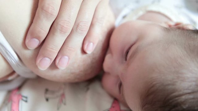 Female hand holding breast next to infant head for breastfeeding, small baby sucking milk