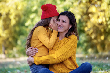 Fototapeta premium Mother and daughter outdoors in a meadow. Daughter whispering to her mother secret.