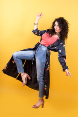 stylish girl in jeans and a lightweight full-length summer coat isolated on a yellow background