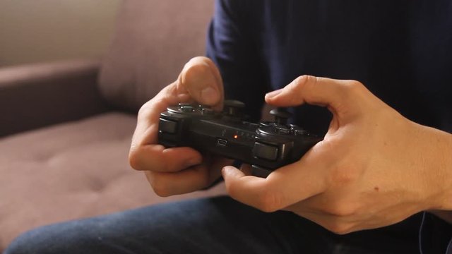 Closeup of man's hands playing video games on gaming console sitting on the couch