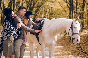 Young family is learning to ride a beautiful white horse in the autumn forest. Riding lesson