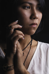 Asian short black haired woman Wearing jewelry made of leather and stone On her face, there is a small freckle On a black background and shadows