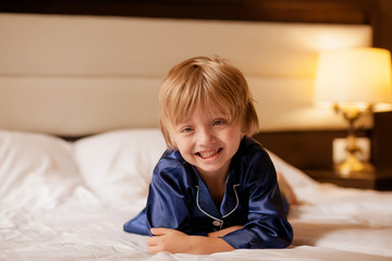 portrait of a happy cute boy 5-6 years old in pajamas, the child lies on a snow-white bed