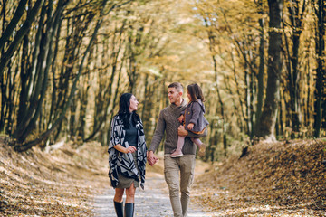 Beautiful young family walking in the autumn forest. Family walking in an autumn park with fallen fall leaves. Warm autumn
