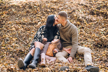 young family in the autumn forest sits on the ground covered with yellow leaves