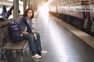 Obraz na płótnie Canvas Long haired man that looks cool He is a traveler or nomadic musician who is backpacking and guitars, walking near train track in rural.