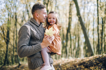 Fototapeta premium Family autumn weekend. Young father and his little daughter together in autumn park outdoors. Beautiful baby with leaves on top of dad.