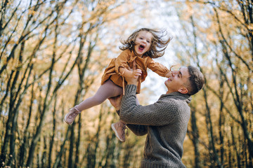 Obraz premium Family autumn weekend. Young father and his little daughter together in autumn park outdoors. Beautiful baby with leaves on top of dad.