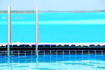 Old swimming pool with ocean view. Shining water. Damaged tiles