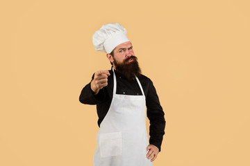 Cook in uniform pointing at you. Professional chef man in cook hat, apron. Serious chef with beard,...