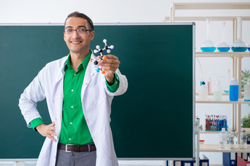 Young male chemist teacher in front of blackboard