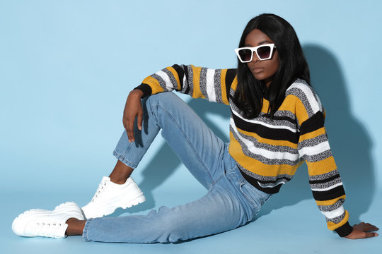 Fashion african model in sweater in stripes sitting on blue background.