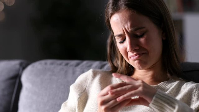 Sad wife complaining looking at wedding ring after divorce sitting on a couch in the 