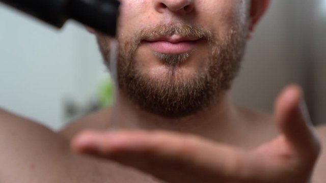 Trendy man pouring barber shampoo on his hand and putting it on his dry beard. Handsome man cleaning facial hair before shaving. Shampoo foam on man's beard, preparation before trimming beard