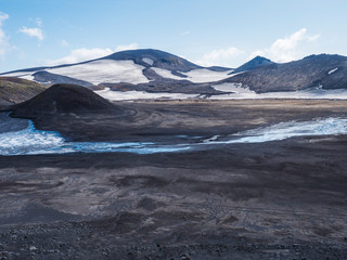 Landscape of Fimmvorduhals hiking trail. Eyjafjallajokull glacier and volcano, lava ash, blue stream from melting snow and ice. Iceland, Summer blue sky