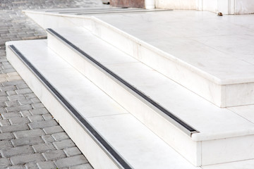 entrance with a marble threshold with stone steps and a white ramp to the exterior on the streets with a pavement of gray tiles.