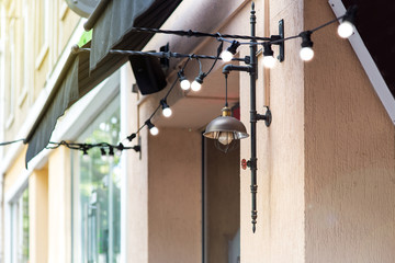 illumination of the facade of the building with a garland of lamps and a wall lantern in the loft style of a pipe and a valve on the building with windows and textile canopies from the sun.