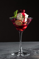Dessert with Cherry Sauce, biscuits and mint in a martini glass on a grey table and black background