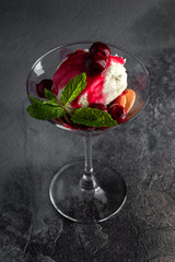 Dessert with Cherry Sauce, biscuits and mint in a martini glass on a grey table and black background. top view