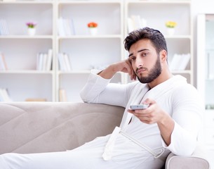 Young man in a bathrobe watching television at home on a sofa co