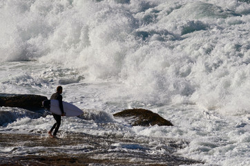 A recreational surfer waits for an opportunity to enter the surf from the rock shelf.
