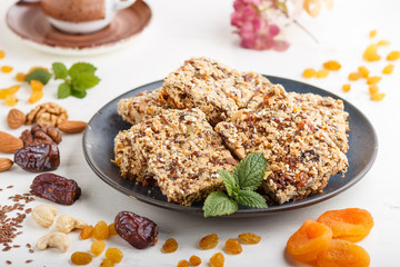 Homemade granola from oat flakes, dates, dried apricots, raisins, nuts in blue ceramic plate on a white wooden background. Side view, selective focus.