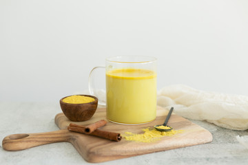 Golden milk with cinnamon, styled on wooden board with loose turmeric, alternative medicine drink, natural healing