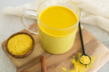 Golden milk with cinnamon, styled on wooden board with loose turmeric, alternative medicine drink, natural healing