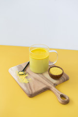 Golden milk styled on wooden board with loose turmeric, alternative medicine drink, natural healing, yellow gold background, copy space