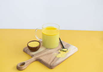 Golden milk styled on wooden board with loose turmeric, alternative medicine drink, natural healing, yellow gold background, copy space