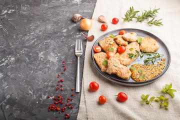 Fried pork chops with tomatoes and herbs on a gray ceramic plate on a black concrete background. side view, copy space.