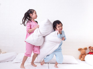 Happy two Asian little cute girls in pajamas playing pillows on the white bed. Two sisters playing...